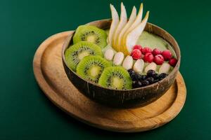 Green smoothie bowl with nuts, kiwi, pear, berry and granola photo