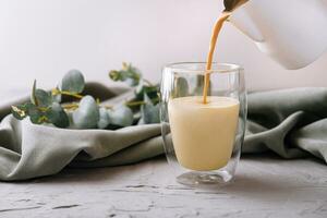 pouring a coffee with milk from teapot to glass cup photo