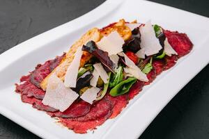 carne de vaca carpaccio con ensalada y parmesano en un blanco plato foto