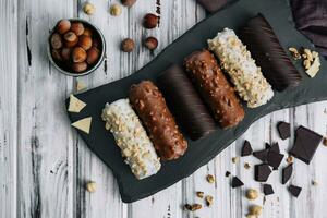 French dessert eclairs or profiteroles with different chocolate icing on a black stone plate photo