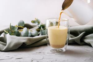 pouring a coffee with milk from teapot to glass cup photo