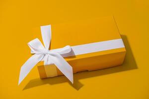 Yellow gift box with white ribbon isolated on yellow photo