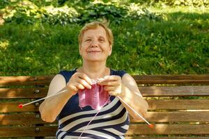 elderly woman happily showing knitting in the park on a sunny day photo