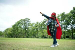 en un hermosa día en el parque, un joven niña disfruta su vacaciones. juguetón con un rojo superhéroe disfraz y mascarilla. foto