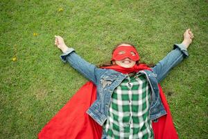 en un hermosa día en el parque, un joven niña disfruta su vacaciones. juguetón con un rojo superhéroe disfraz y mascarilla. foto