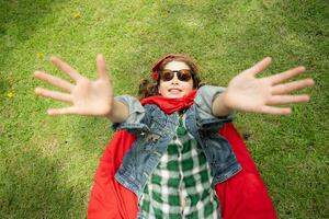 On a beautiful day in the park, a young girl enjoys her vacation. Playful with a red superhero costume and mask. photo