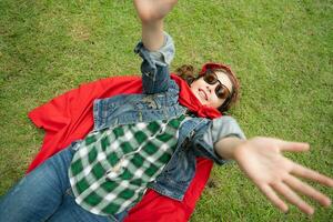 On a beautiful day in the park, a young girl enjoys her vacation. Playful with a red superhero costume and mask. photo