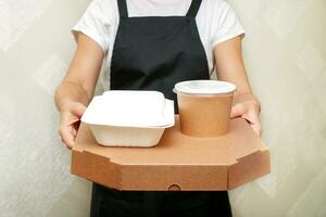 un mujer café trabajador sirve un terminado para llevar orden en caja Pizza y un envase con aperitivos y sopa en desechable utensilios hecho desde reciclado crudo materiales foto