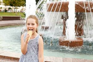 pequeño linda niña comiendo hielo crema por el fuente foto