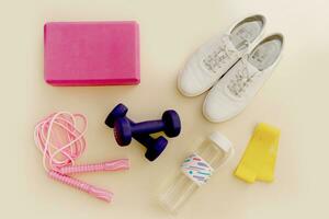 sneakers, jump rope, water bottle, elastic band for fitness, dumbbells and a yoga brick on a light background. photo