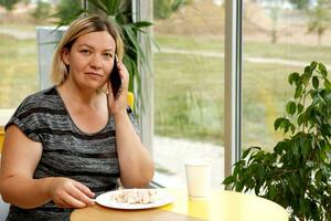 mujer en un café come postre y negociaciones en el teléfono a el mismo hora foto