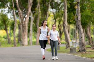 joven hembra y pequeño niña con caminando ejercicios en el ciudad parque foto