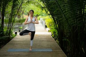 joven hembra en el jardín allí son de madera pasarelas y un túnel de Fresco verde árboles, con yoga ocupaciones para salud foto