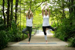 joven hembra y pequeño niña discípulo en el jardín allí son de madera pasarelas y un túnel de Fresco verde arboles con yoga ocupaciones para salud foto