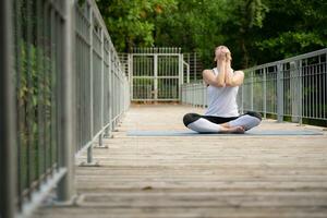 Young female on a wooden bridge in the park with healthy yoga activities photo