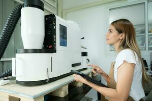 Young woman in apron using digital tablet for checking quality of of coffee beans with digital roaster photo
