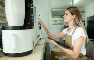 Young woman in apron using digital tablet for checking quality of of coffee beans with digital roaster photo