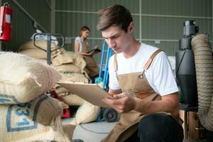 Portrait of a young male worker in overalls working checking coffee beans bag in a coffee beans warehouse photo