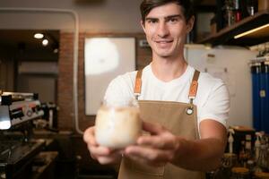 barista participación un vaso de frío latté café en su manos a cliente foto
