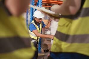 almacén trabajadores trabajo juntos en un grande depósito. un masculino empleado es exploración el contenido de un caja en un máquina elevadora. foto