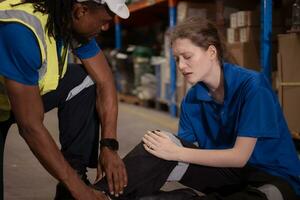 A warehouse worker consoles and helps a female worker who cries out in pain after a leg accident in a large warehouse photo