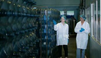 Two female workers in white coats standing at the drinking water factory with bottles of water photo