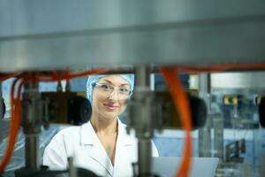 Female scientist in white coat and blue hat working in the control  machine of production line. photo