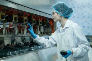 Female scientist in white coat and blue hat working in the control  machine of production line. photo