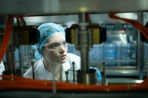 Female scientist in white coat and blue hat working in the control  machine of production line. photo