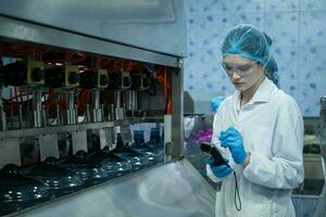 Female scientist in white coat and blue hat working in the control  machine of production line. photo