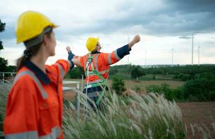 Young female engineer working in a wind turbine field and young man engineer wear a safety vest raise both hands to relax after finishing the wind turbine inspection mission photo