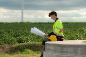 Young engineer working on a wind turbine field looking at the blueprint in the middle of the black clouds with sunlight shining, The concept of natural energy from wind. photo