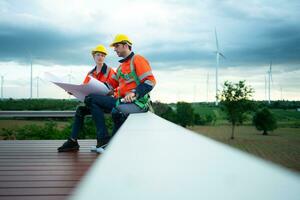 Engineer and technician discussing blueprint on the building site with wind turbine background photo