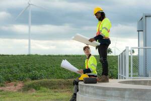 Engineers and technicians work together on the tower base of a large wind turbine with a wind turbine field in the background, The concept of natural energy from wind. photo