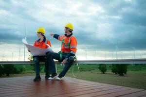 Engineer and technician discussing blueprint on the building site with wind turbine background photo