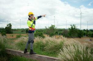 Engineer in a yellow helmet and reflective vest on the background of wind turbines using walkie talkie for communication photo