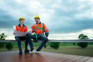Engineer and technician discussing blueprint on the building site with wind turbine background photo