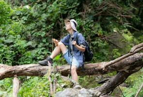 Young man traveler sitting on a fallen tree and looking at the compass in hand. photo