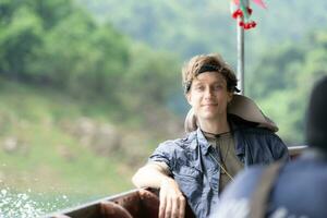 A young man sits on a boat for a journey into the forest above the dam for trekking. photo