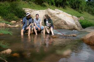 Group of friends sitting on the rock in the middle of the river. Rest during the hiking in the forest. photo