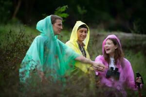 Group of friends in raincoats with backpacks on a hike in the forest, Prepare to hiking after the rain has stopped. photo