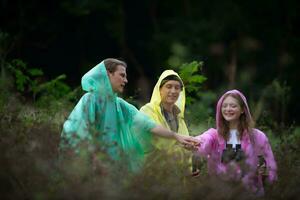 Group of friends in raincoats with backpacks on a hike in the forest, Prepare to hiking after the rain has stopped. photo