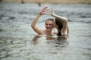 Two young girls in the water making a heart with their hands. photo