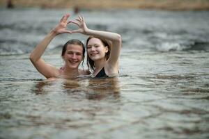 Two young girls in the water making a heart with their hands. photo