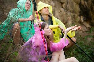 grupo de amigos en impermeable con mochilas excursionismo en el bosque, sentar y abrigo desde el lluvia foto