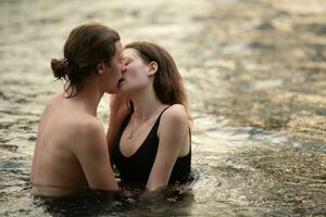 joven Pareja besos en el medio de el río fluido en frente de el cámping. foto