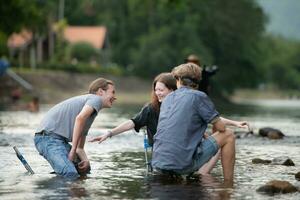 grupo de amigos son hablando y teniendo divertido en el medio de el río fluido en frente de el cámping. foto