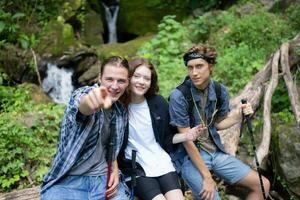 grupo de amigos con mochilas y palos sentado en un caído árbol, tomar un descanso durante el caminata foto