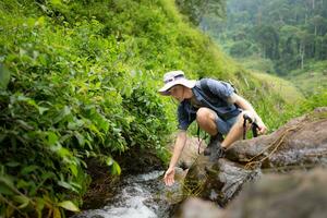 Hiker in the jungle playing with water in a stream in the forest. photo