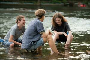grupo de amigos son hablando y teniendo divertido en el medio de el río fluido en frente de el cámping. foto